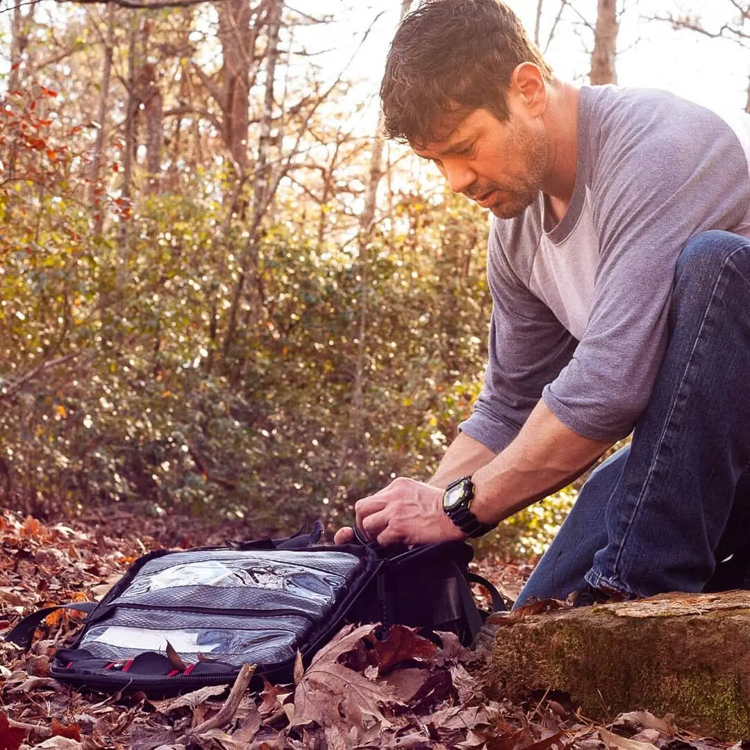 Man kneeling in autumn woods beside an open gear bag